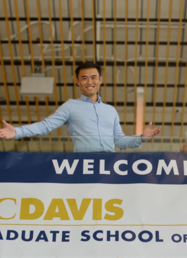 Two individuals posing in front of UC Davis Graduate School of Management banner