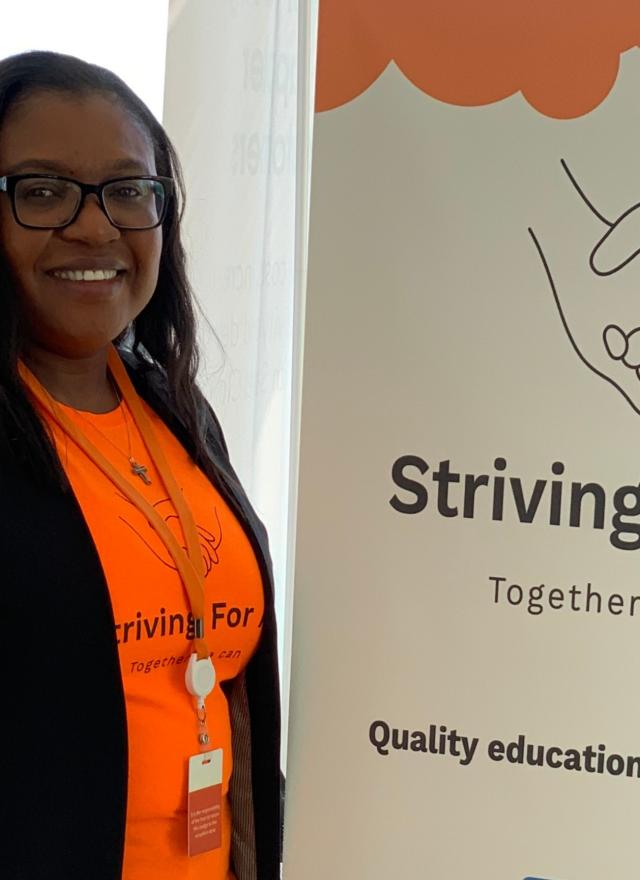 Genevieve Ngambia standing next to a sign with the name of the nonprofit she founded