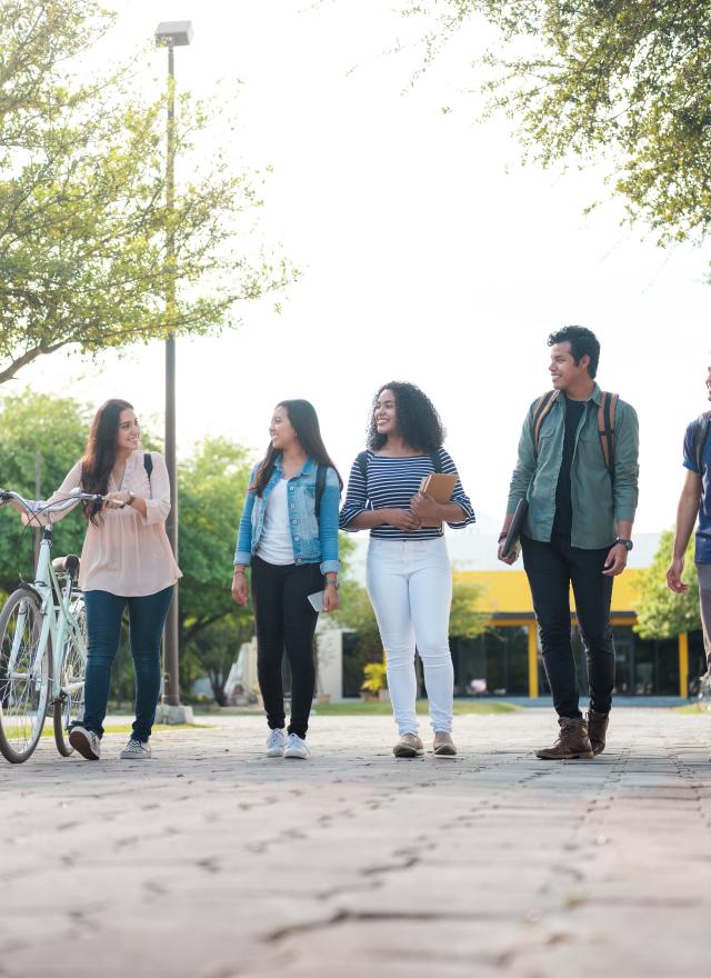 A group of student friends walking together after class carrying books and laptops.