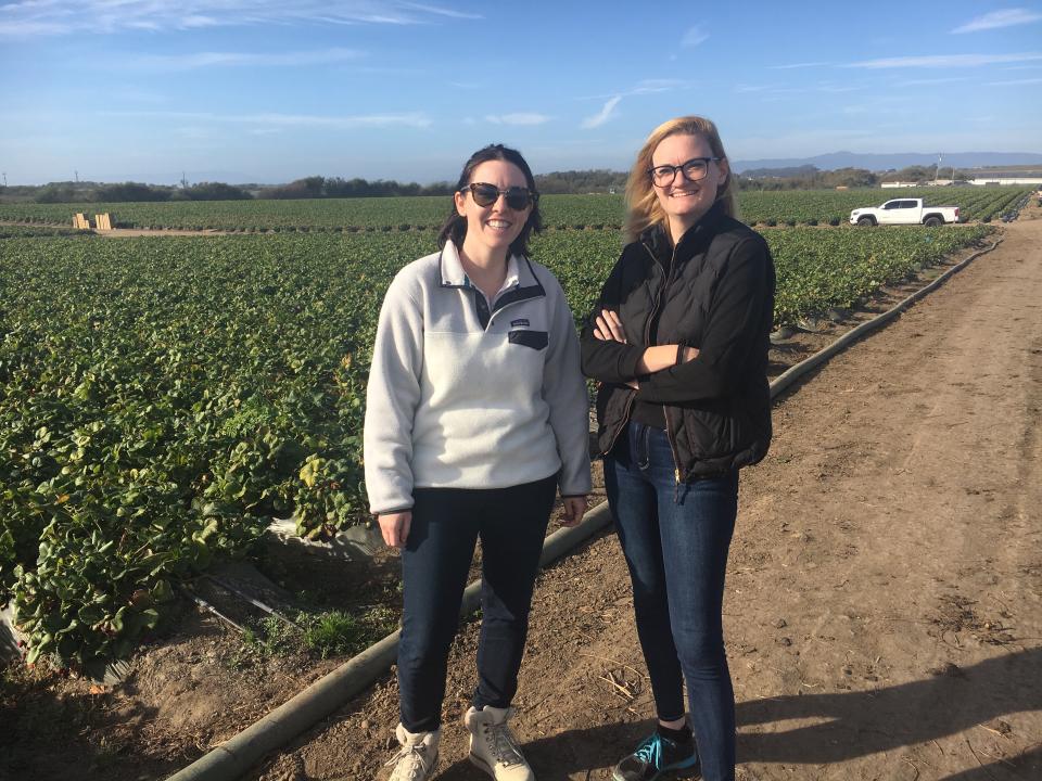 Two women standing on a dirt road next to a field