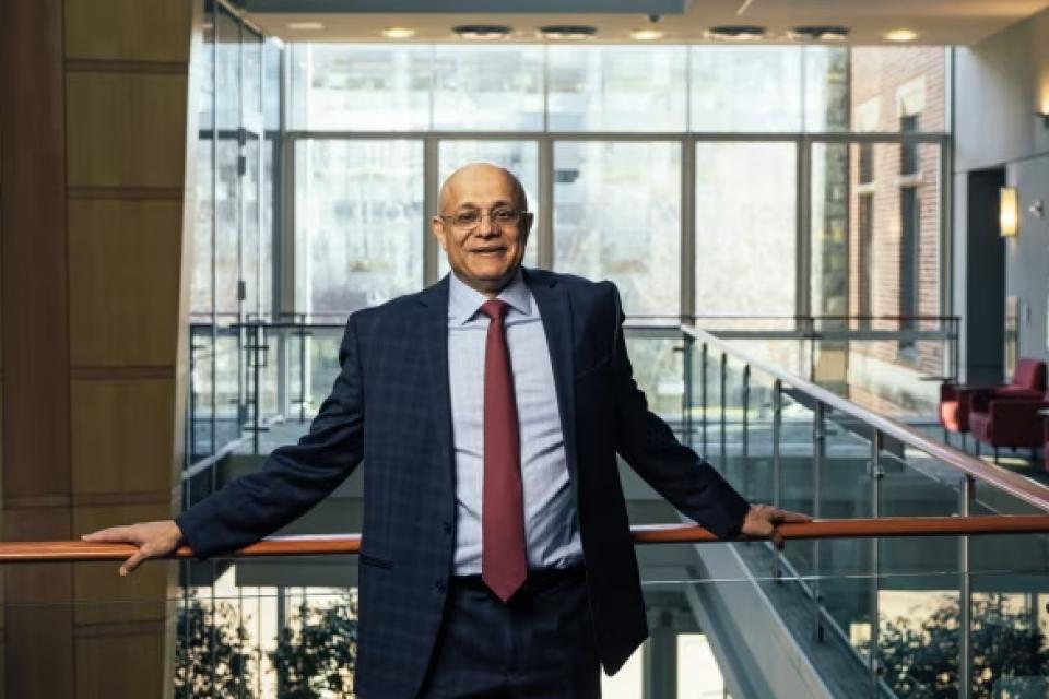 photo of a man in glasses, leaning against a balcony